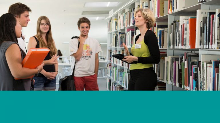 Une bibliothécaire répond aux questions des étudiants dans les rayonnages dans la Bibliothèque