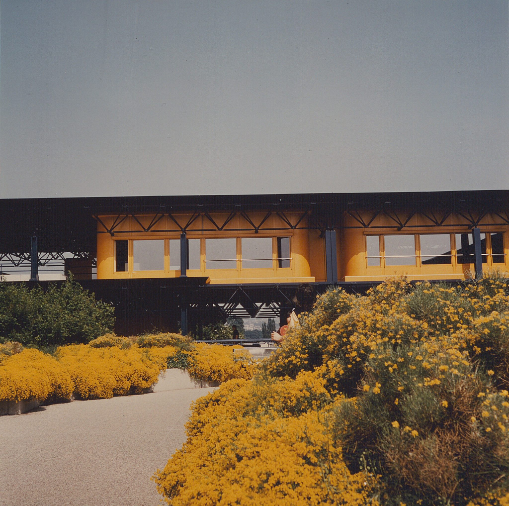 Photographie des terrasses de l'EPFL. Les fleurs orange débordent abondamment des bacs et leur couleur se confond avec celle de la façade.